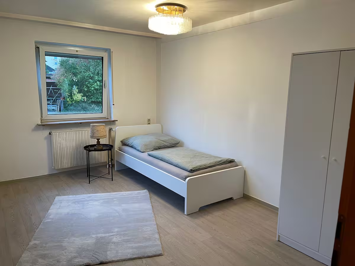 Helles Einzelzimmer mit Bett, Kleiderschrank und Fenster